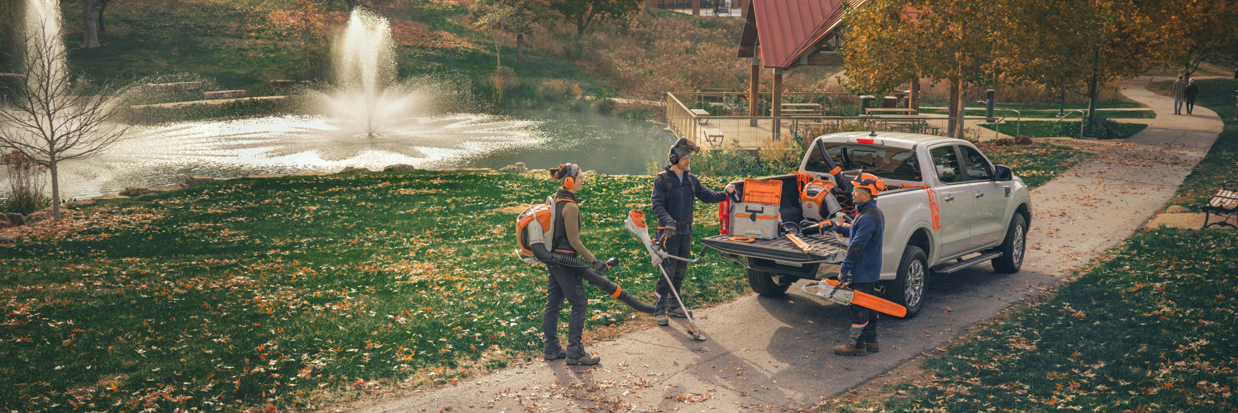  Un groupe de paysagistes professionnels se tient autour de leurs véhicules et se prépare à travailler avec des appareils à batterie STIHL.