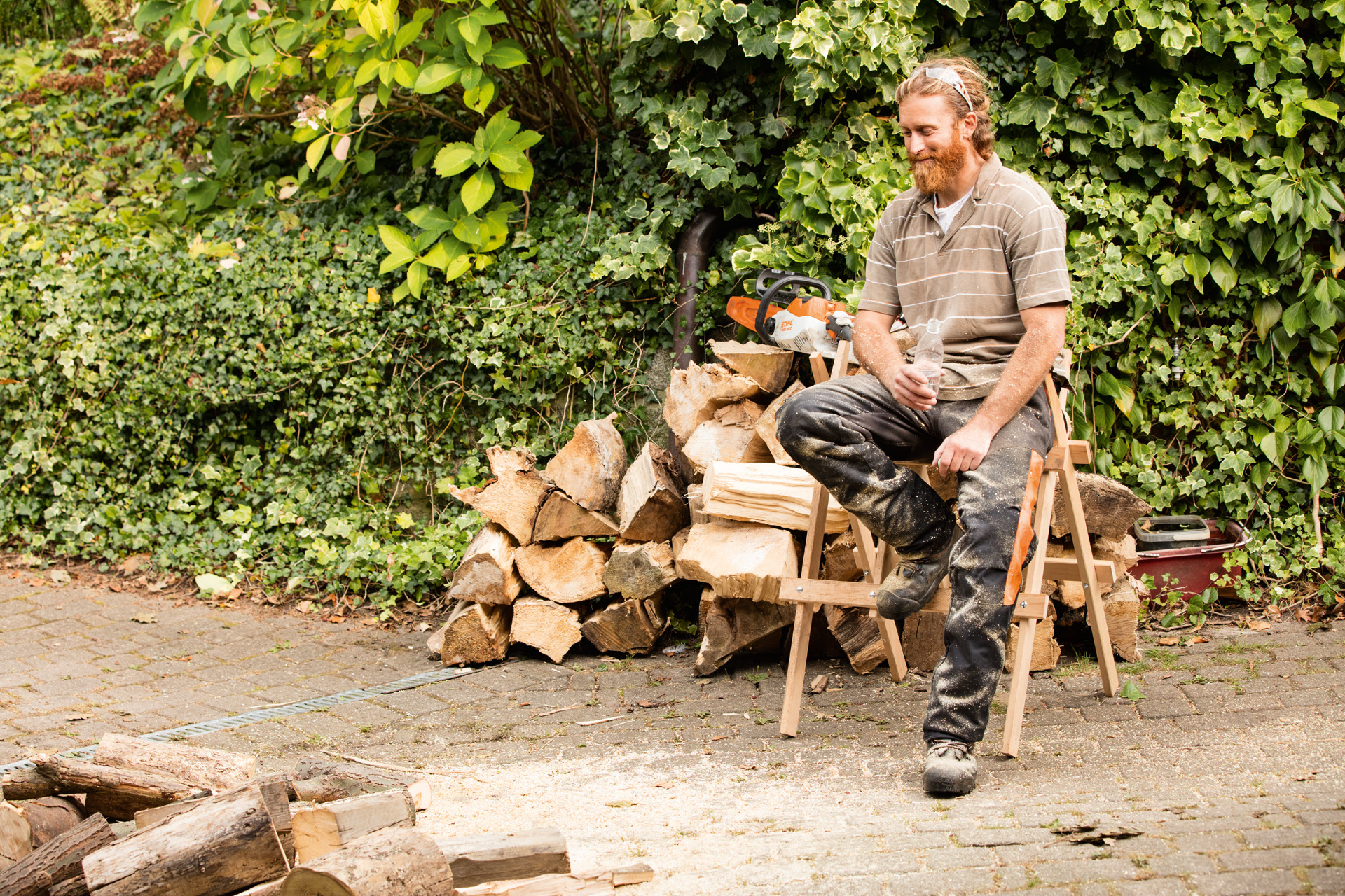 Mann vor Holzscheit sitzend auf einem Sägebock.