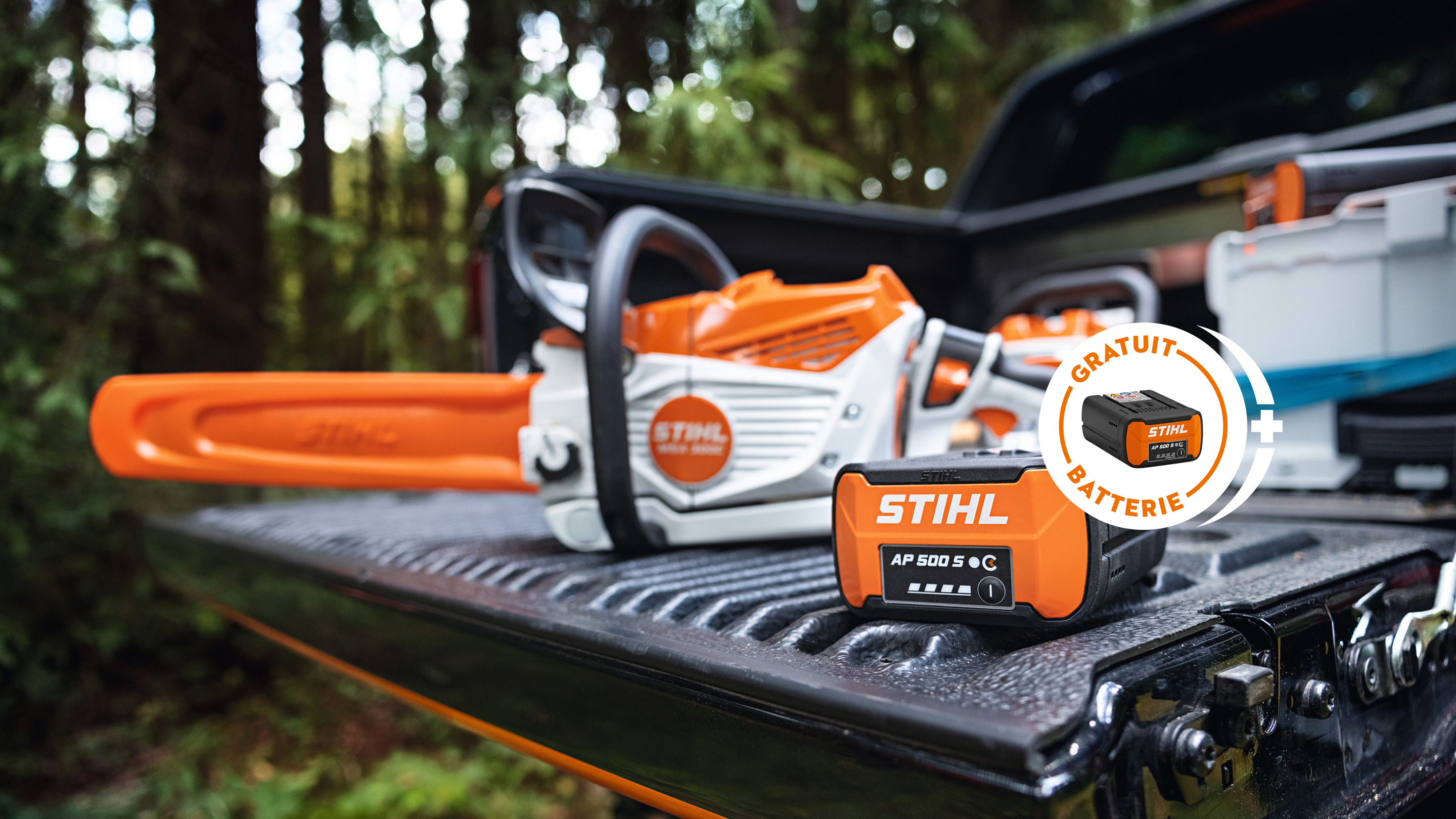 Batterie STIHL AP 500 S dans la benne d’un pick-up avec la nouvelle tronçonneuse à batterie STIHL MSA 300, avec une affiche d’une batterie STIHL portant l’inscription « batterie gratuit».