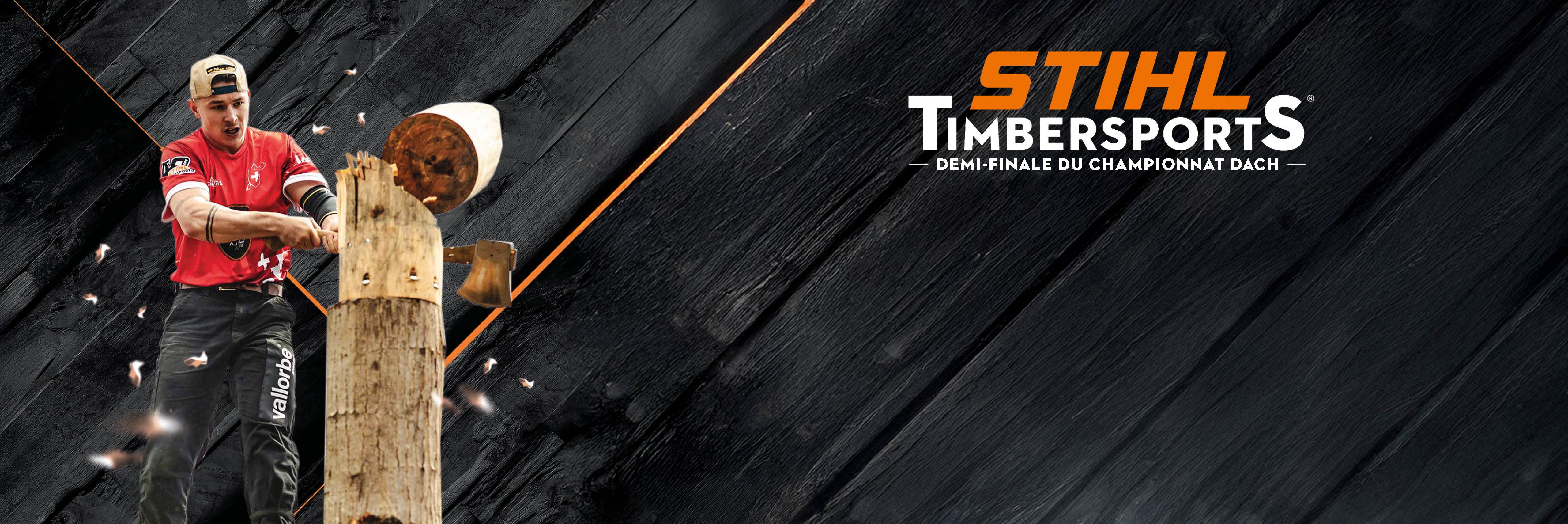 Athlète en tenue de compétition rouge lors de STIHL TIMBERSPORTS®, coupant un tronc de bois debout avec une hache, tandis que des copeaux de bois volent dans les airs. Arrière-plan sombre avec une structure diagonale et des lignes orange.