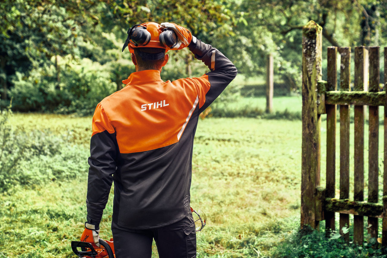 Rückseite eines Mannes in der STIHL Function Core Jacke mit Kopf- und Gehörschutz