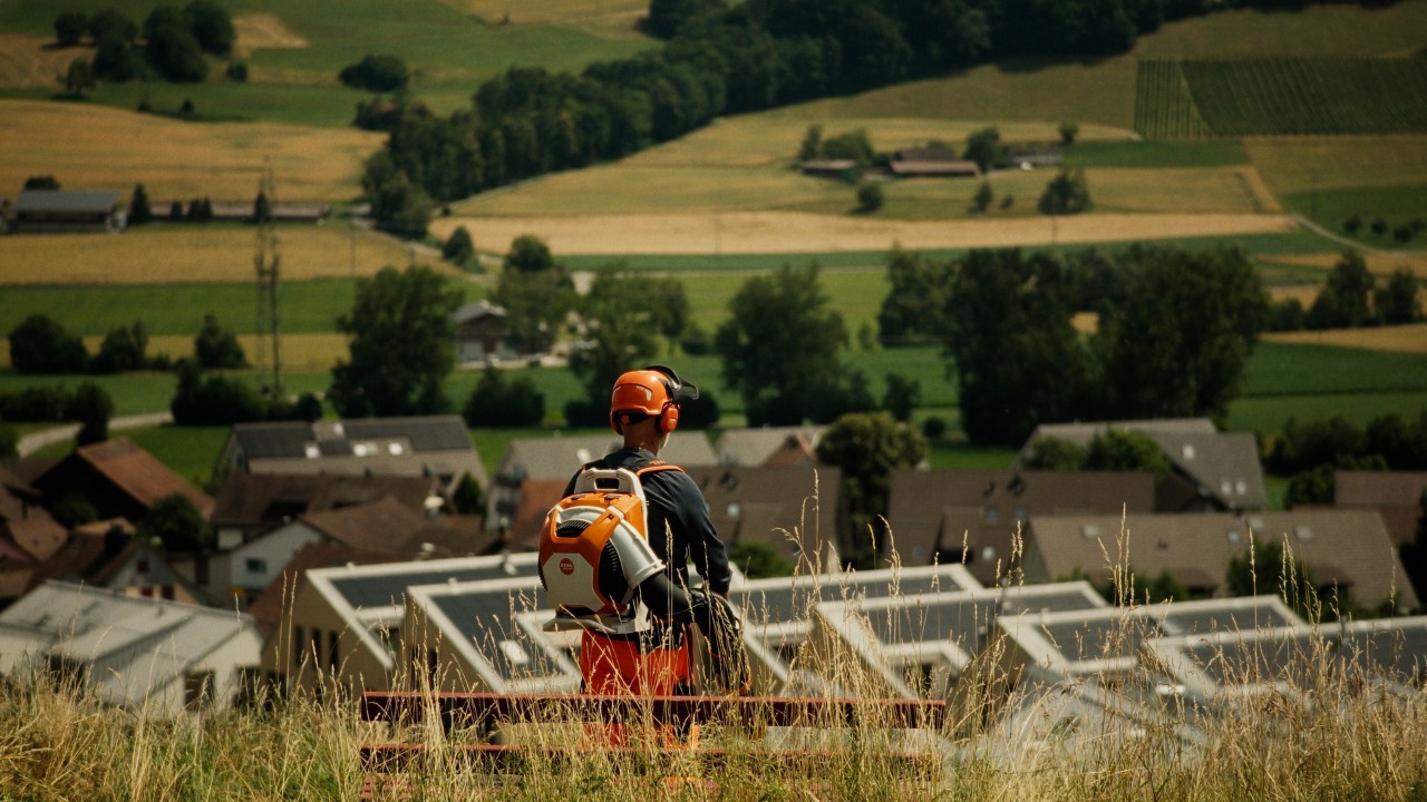 Lukas blickt auf die Gemeinde und trägt ein STIHL Blasgerät BRA 600 auf dem Rücken, Real People. STIHL People. Kampagne