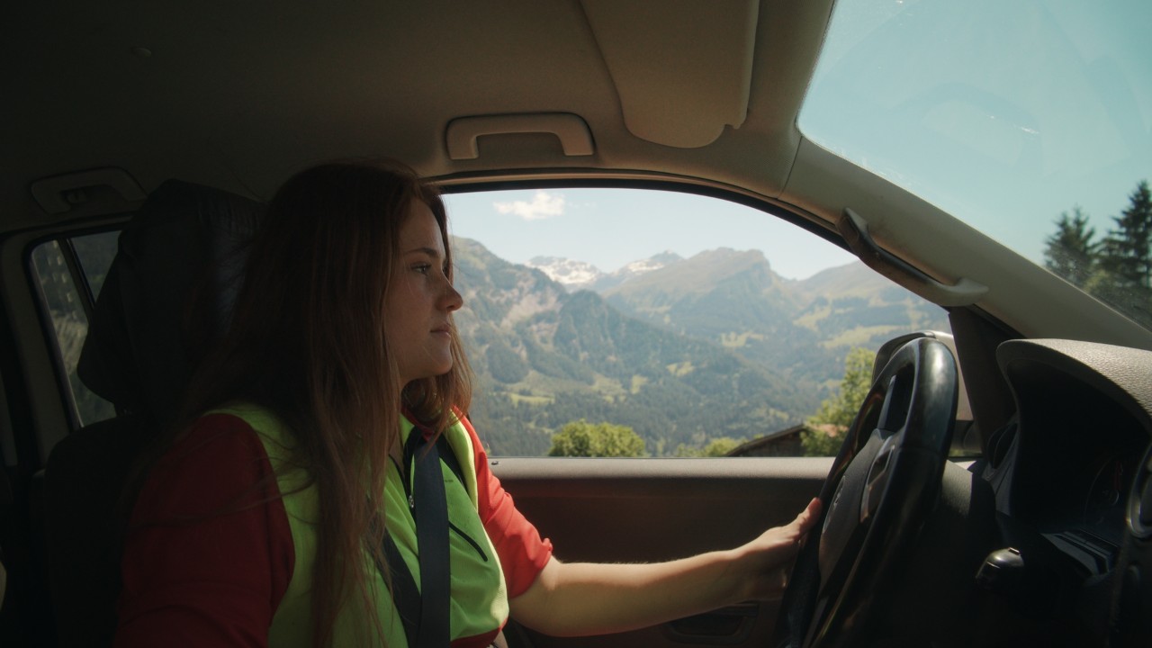 Bigna fährt ein Auto durch eine alpine Landschaft, Blick aus dem Fahrzeuginnenraum auf Lenkrad und Bergpanorama, Real People, STIHL People