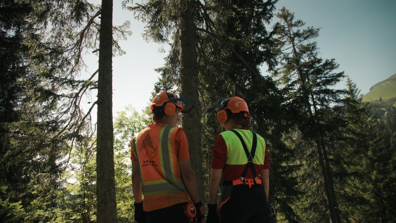 Bigna und ein Teammitglied aus ihrem Forstbetrieb in Schutzausrüstung im Wald vor einem Baum, "Real People. STIHL People." Kampagne