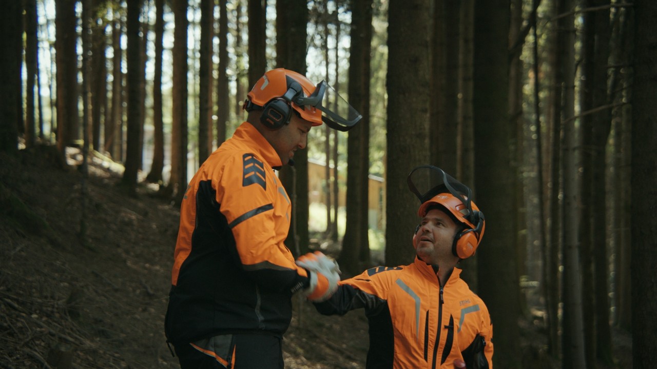 Daniel und ein Freund im Wald beim High Five nach der Holzarbeit, mit Schutzausrüstung von STIHL, Real People. STIHL People. 