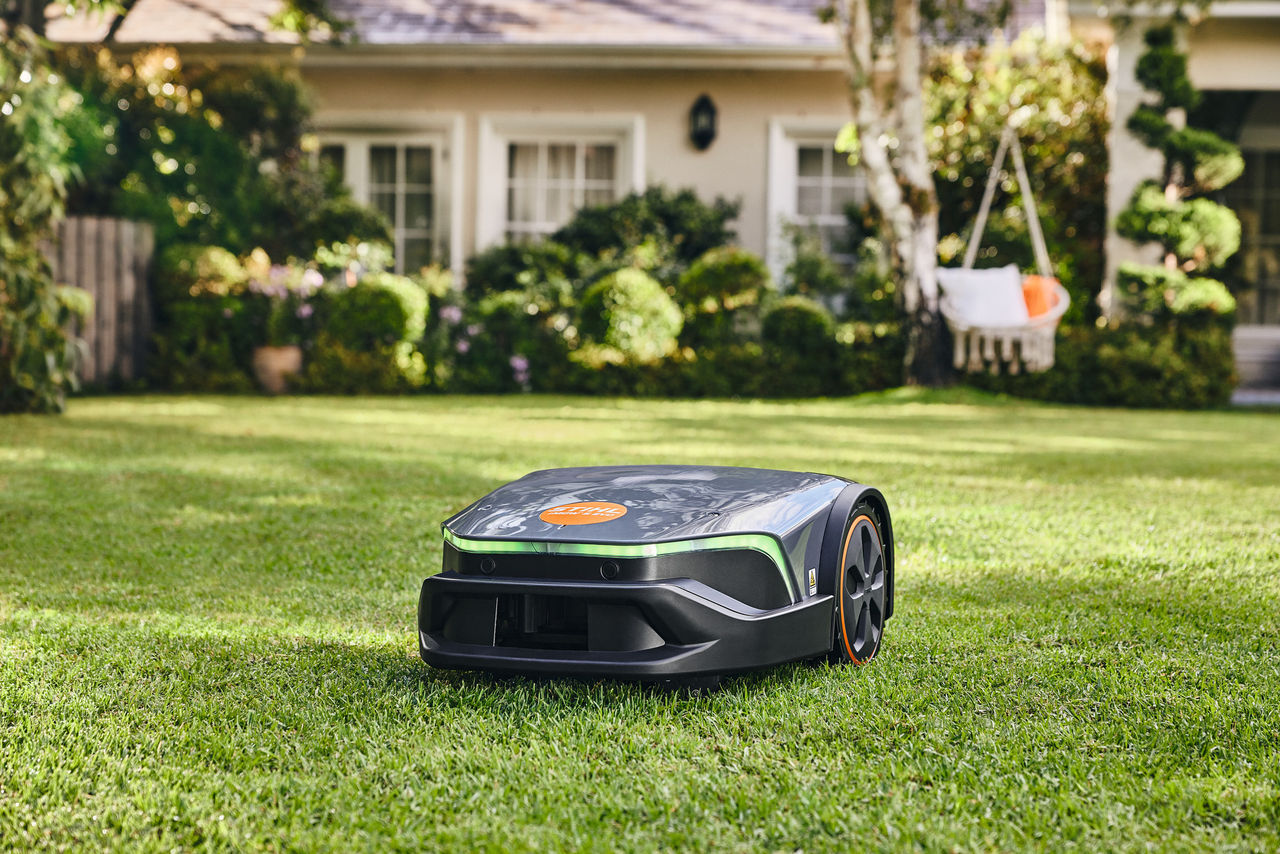 Ein iMOW® Evo Rasenmähroboter mäht im Garten vor einem Haus und einer Hängematte den gut gepflegten Rasen.