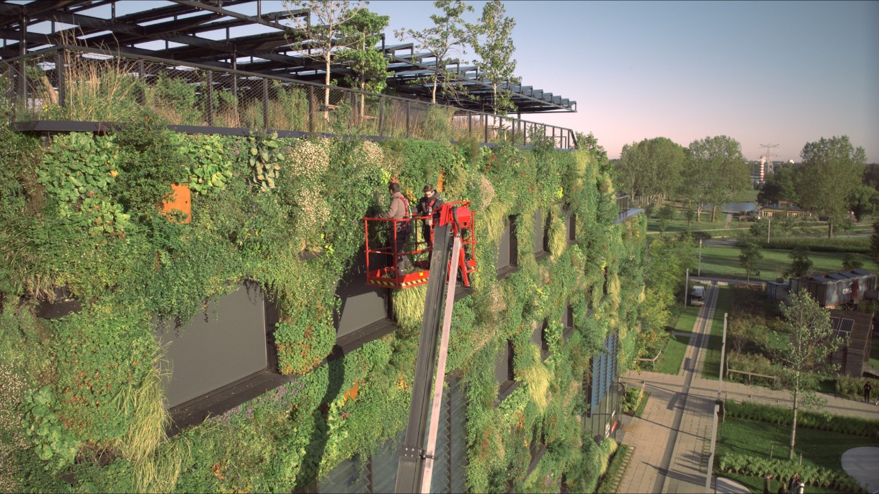 Deux travailleurs sur une plate-forme élévatrice s'occupent de la verdure sur le campus de l'Aeres Hogeschool.