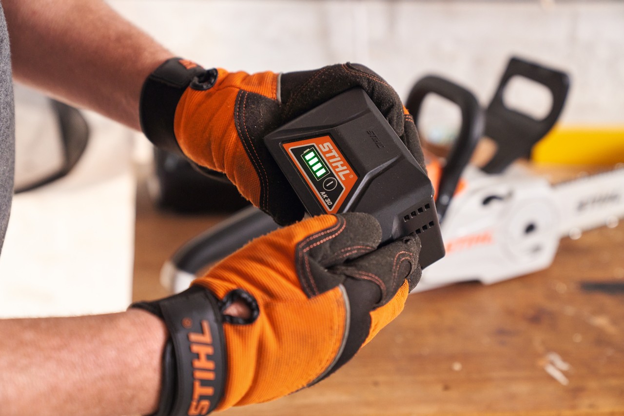 Personne portant des gants de protection STIHL tenant une batterie au lithium-ion STIHL.