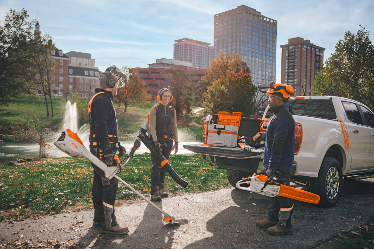 Un groupe de paysagistes professionnels, rassemblés autour de leurs véhicules, se préparent à travailler avec des outils sans fil STIHL.