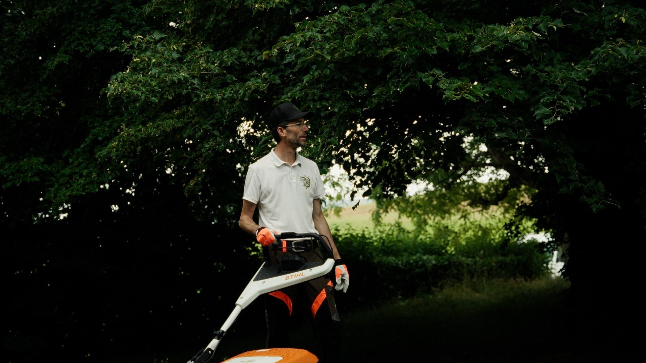 Patrick si trova in giardino con un tosaerba STIHL e guarda il prato, campagna Real People. STIHL People.