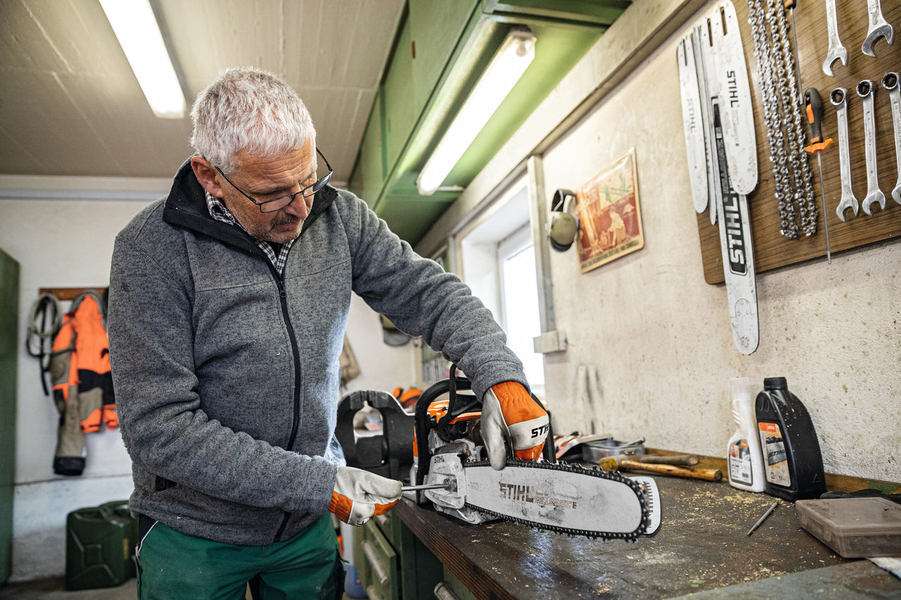Un uomo in un'officina avvita su una motosega la spranga di guida STIHL Rollomatic E 
