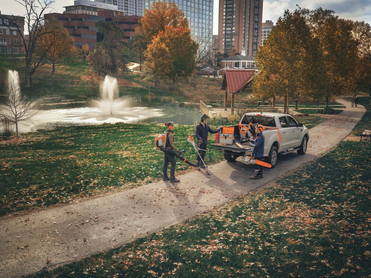 Un gruppo di paesaggisti professionisti è riunito attorno ai propri veicoli, pronto a mettersi al lavoro con gli utensili a batteria STIHL.
