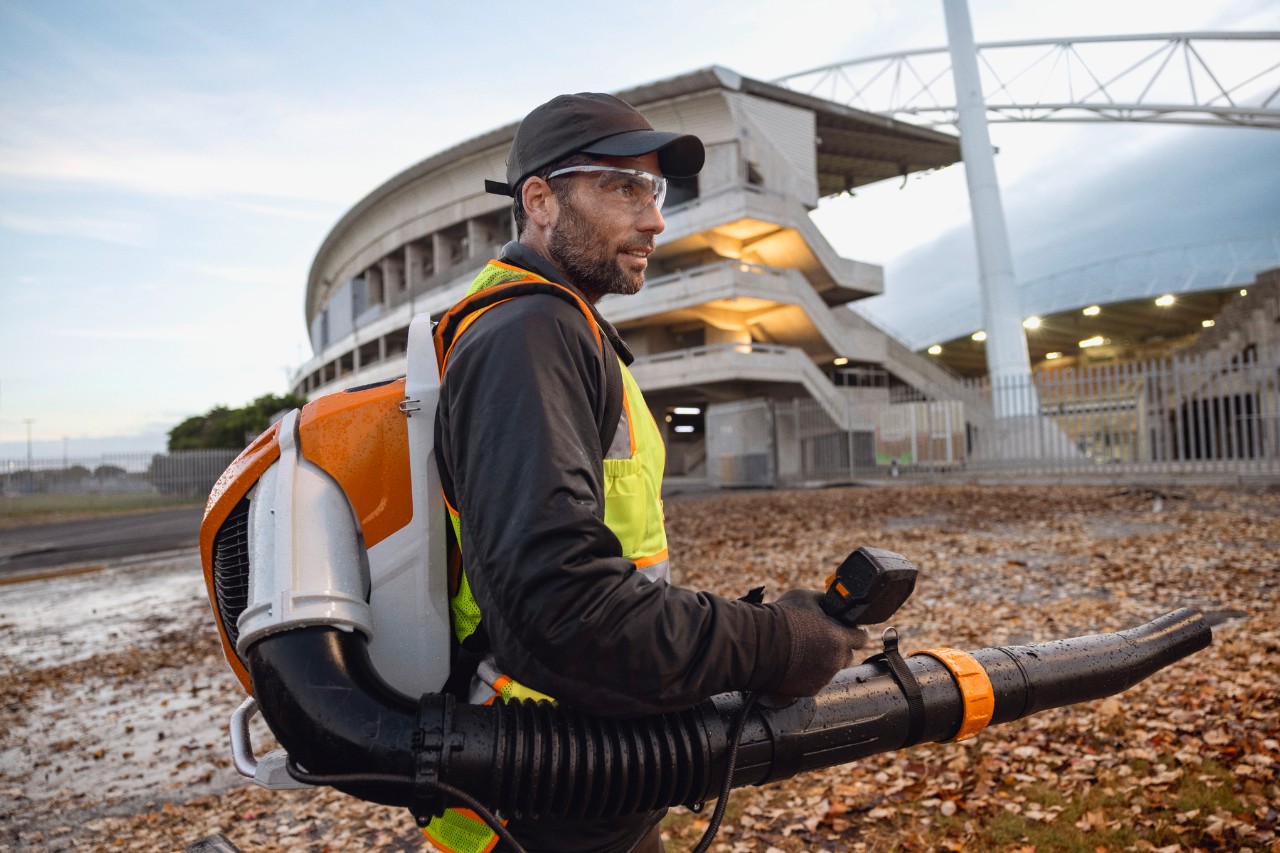 A tarda sera, una persona sta ripulendo uno stadio da foglie e detriti utilizzando il soffiatore a batteria ALLPRO STIHL BRA 600.