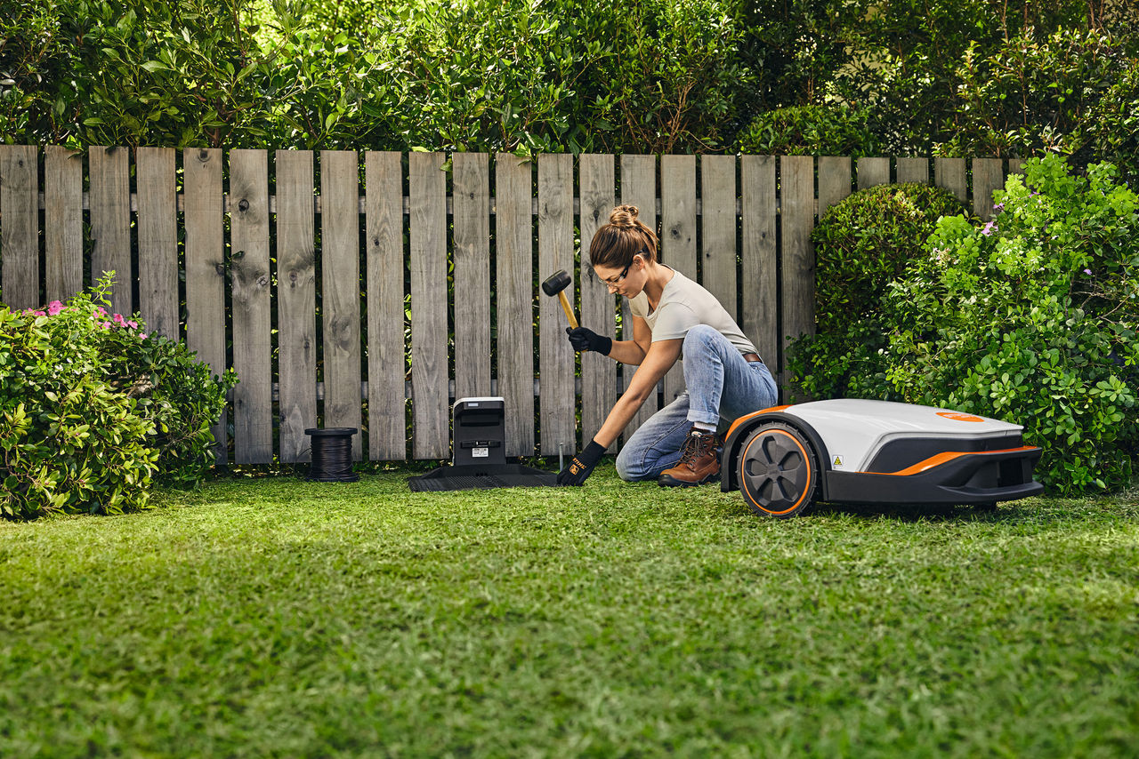 Donna che installa la docking station iMOW® su un terreno da giardino con un martello in mano