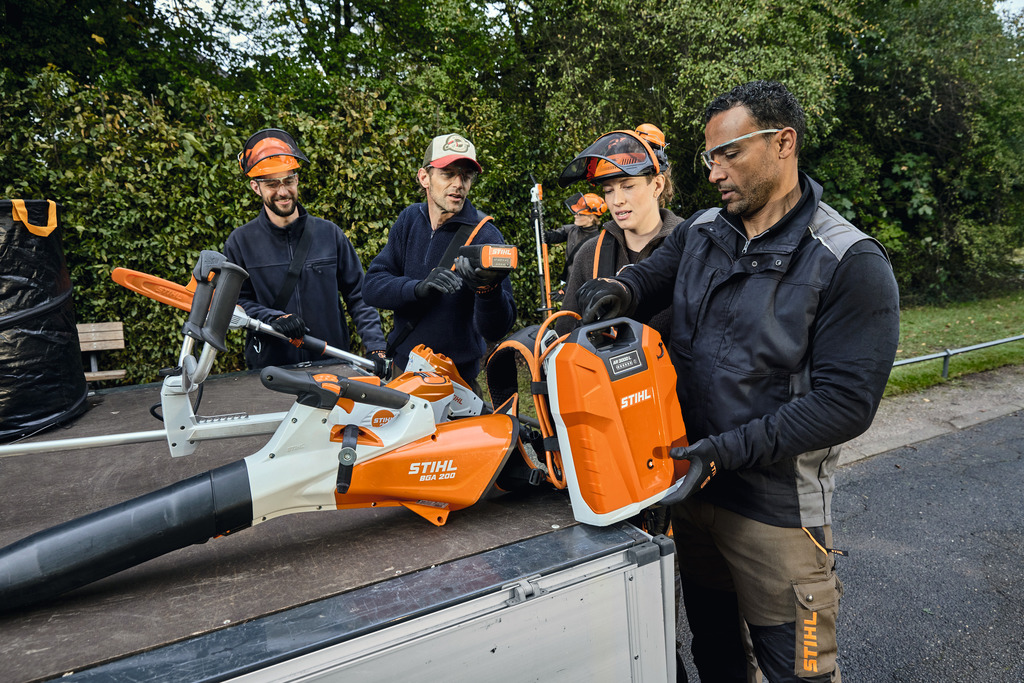 Una squadra di professionisti del paesaggismo scarica le proprie attrezzature professionali STIHL alimentate a batteria dal vano di carico di un veicolo.