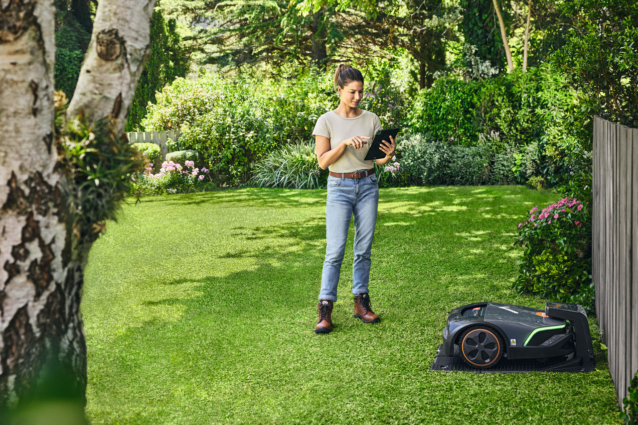 Frau bedient den STIHL iMOW® EVO über ein Tablet in ihrem Garten
